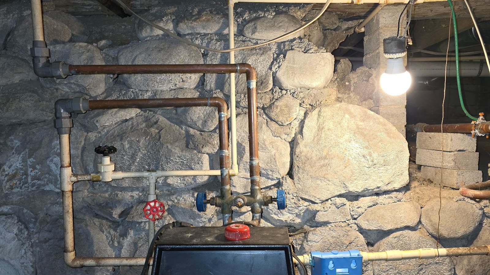 Older residential plumbing lines and filtration equipment in a stone basement